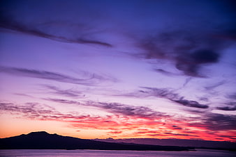 Vibrant purple and orange sunset over ocean and mountains