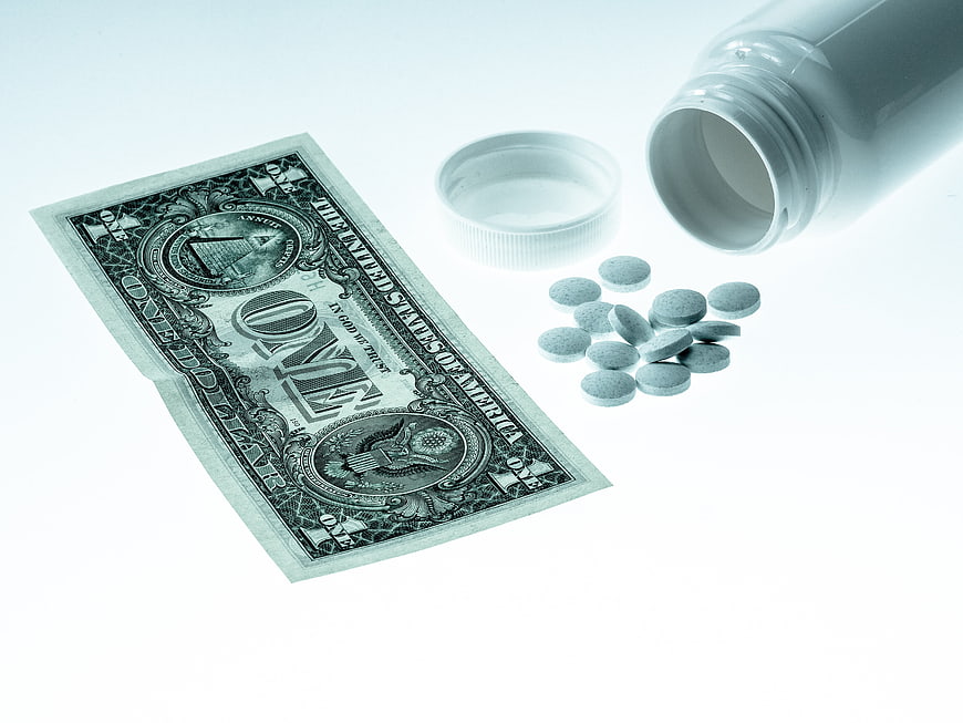 One Dollar Bill And Spilled Medicine Pills On White Background