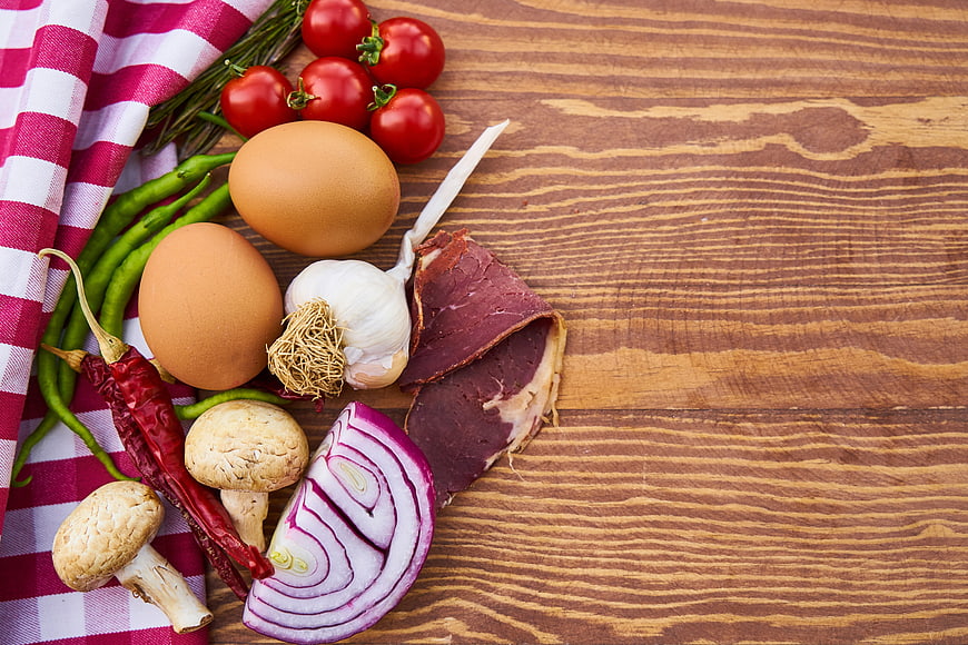 Fresh raw ingredients including eggs, meat, and vegetables on a wooden table
