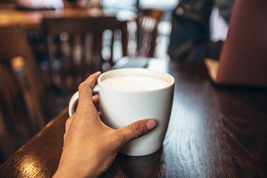 Hand Holding White Coffee Cup on Wooden Table