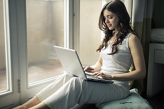 Woman in pajamas using laptop by window