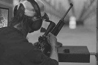 Man aiming scoped rifle at indoor shooting range