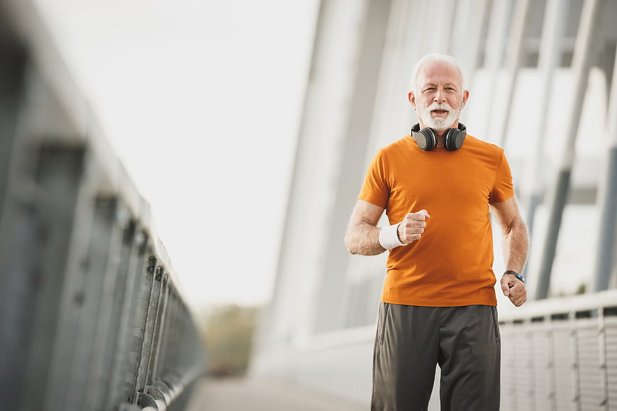 Senior man jogging on bridge with headphones