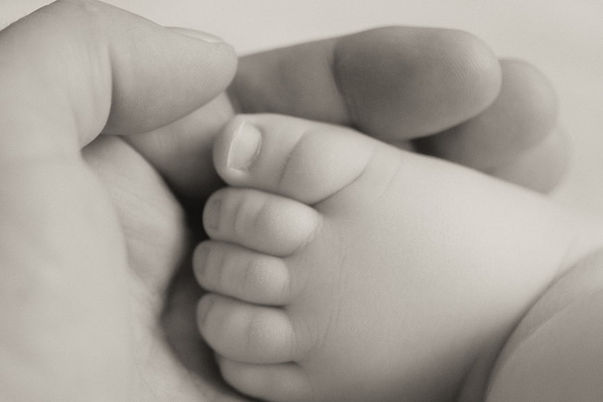Close-up of Adult Hand Holding Newborn Baby Foot