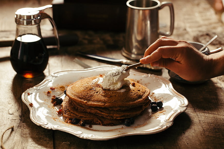 Stack of pancakes with whipped cream and blueberries on rustic table