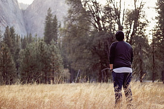 Man standing in tall grass field looking at forest and mountains