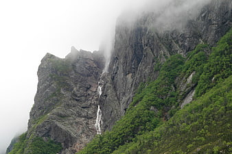 Misty waterfall cascading down steep rocky mountain cliff