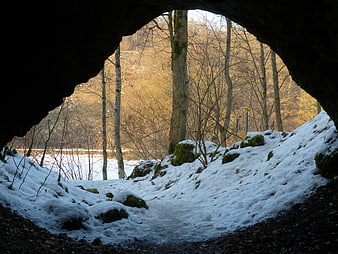 Snowy Forest Path Viewed Through Dark Cave Entrance