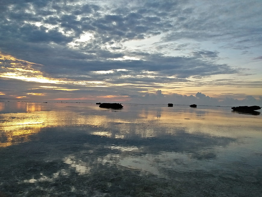 Serene sunset over calm ocean with scattered rocks and reflections