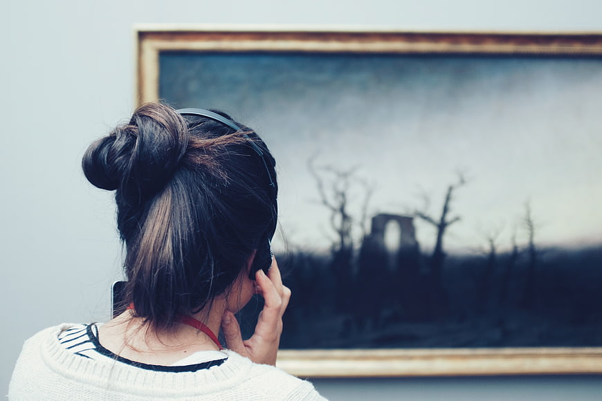 Woman with headphones viewing painting in art gallery