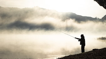 Silhouette of fisherman casting rod on misty lake morning