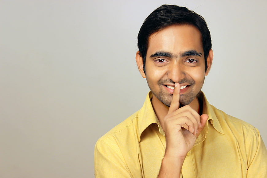 Young man in yellow shirt making shush gesture against gray background