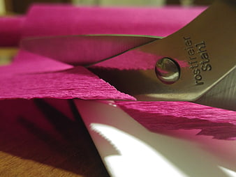 Close-up of metal scissors cutting vibrant pink textured paper