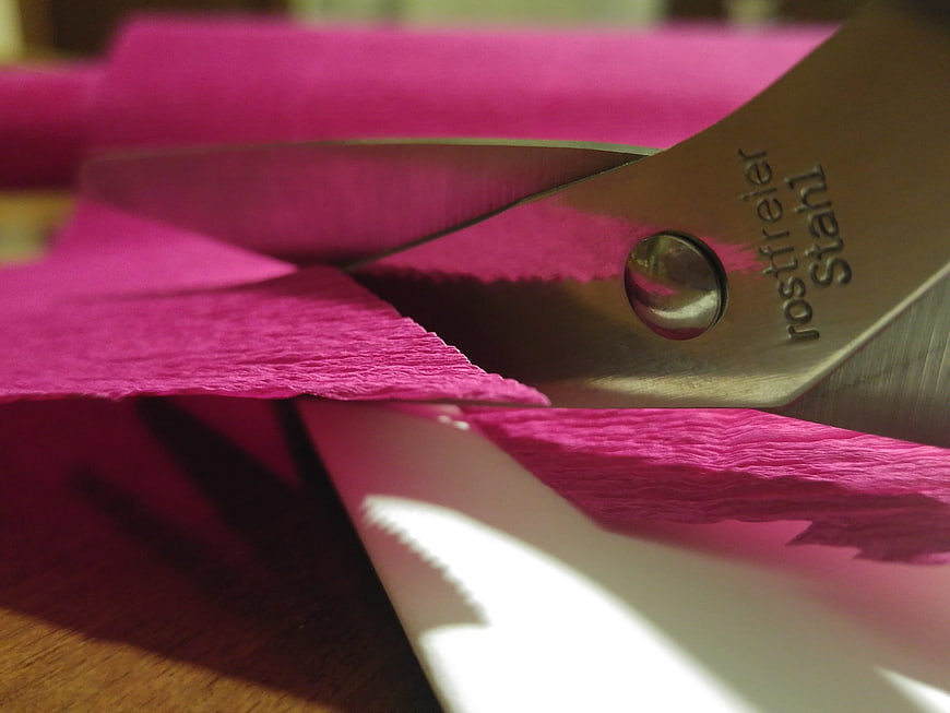 Close-up of metal scissors cutting vibrant pink textured paper