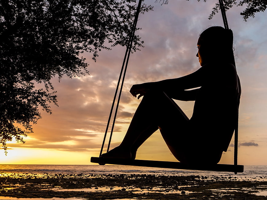 Silhouette of Woman on Beach Swing at Sunset