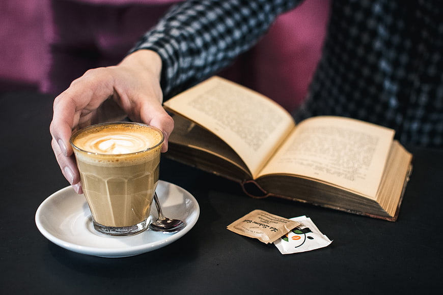 Hand holding latte coffee cup with open book on table