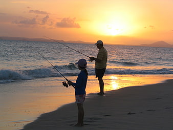 Father and daughter fishing on a beach at sunset