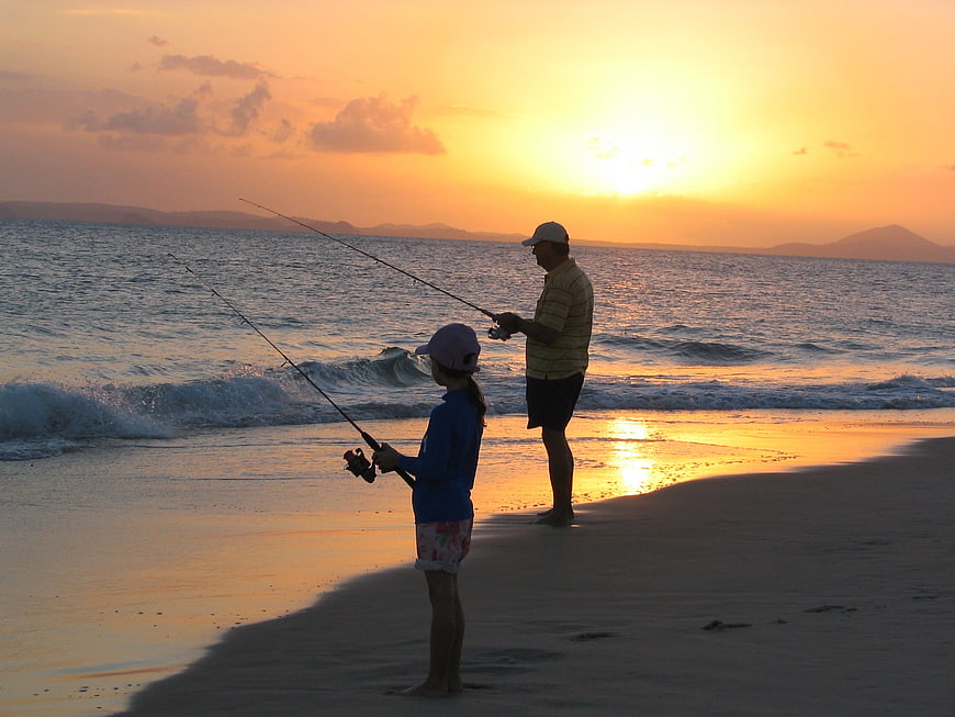 Father and daughter fishing on a beach at sunset