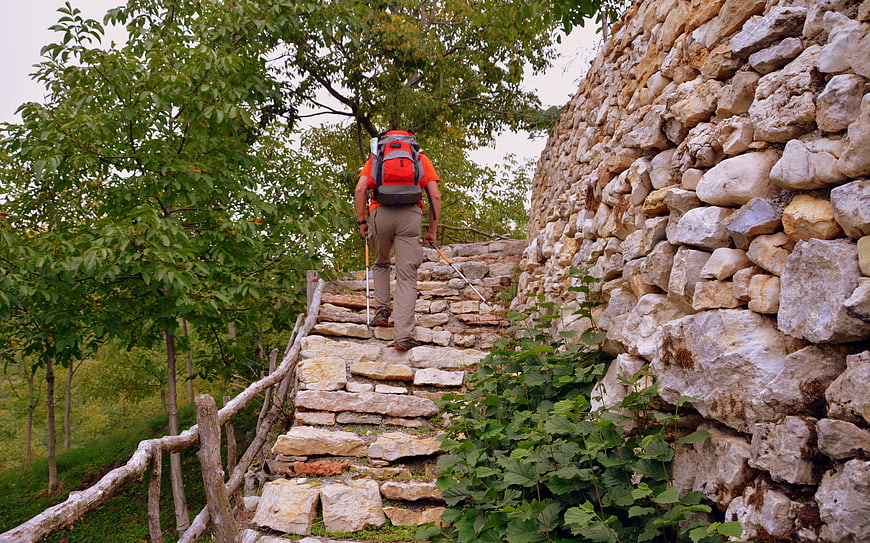 Hiker with backpack climbing stone steps in Lessinia, Italy