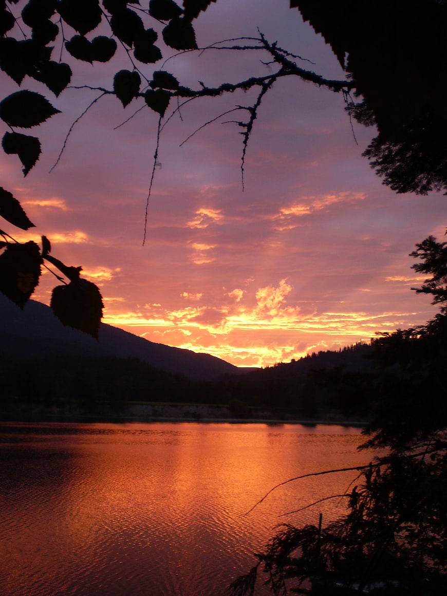 Vibrant sunset over river with silhouetted trees and mountains