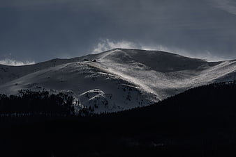 Dramatic Snow-Covered Mountain Peak with Dark Forest Foreground