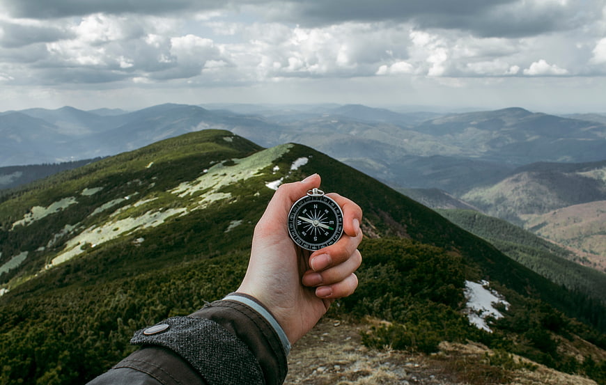 Hand Holding Compass on Mountain Ridge with Panoramic View