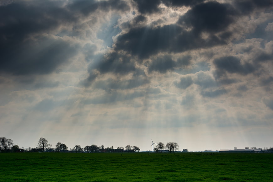 Dramatic Sunbeams Breaking Through Storm Clouds Over Green Field