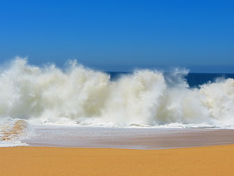 Powerful Ocean Waves Crashing on Sandy Beach Under Blue Sky