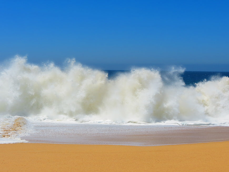 Powerful Ocean Waves Crashing on Sandy Beach Under Blue Sky