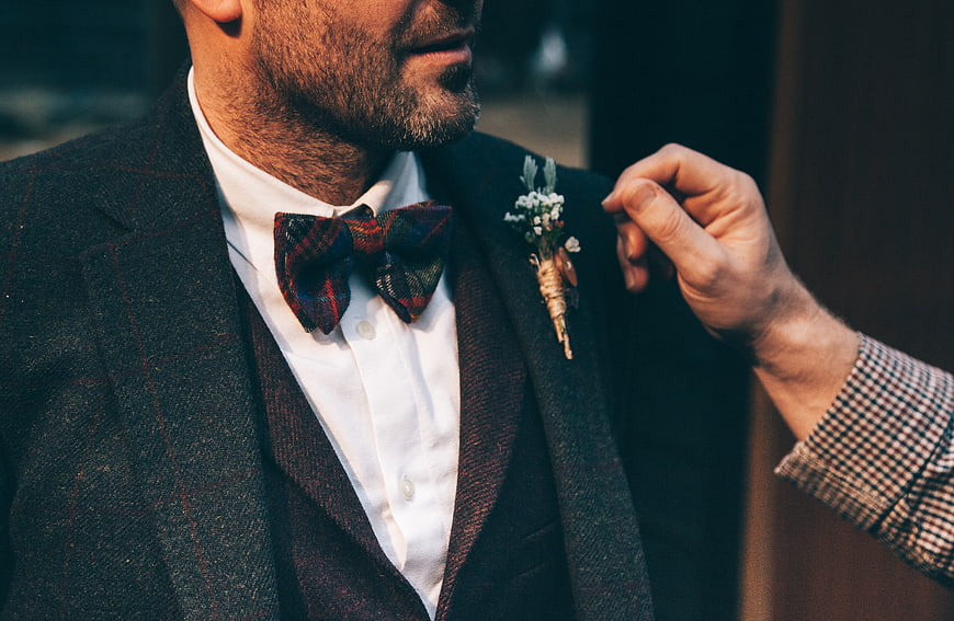 Groom adjusting boutonniere on plaid suit lapel