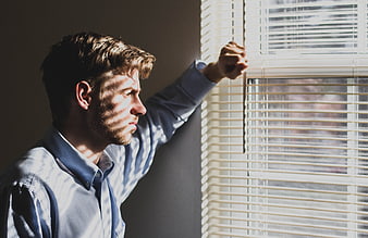 Man looking through window blinds in sunlight