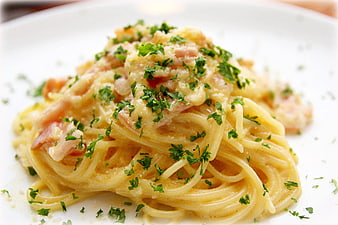 Close-up of creamy spaghetti carbonara with fresh parsley and bacon on a white plate