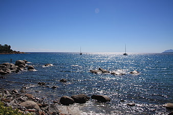 Sailboats on Sparkling Blue Sea with Rocky Shoreline
