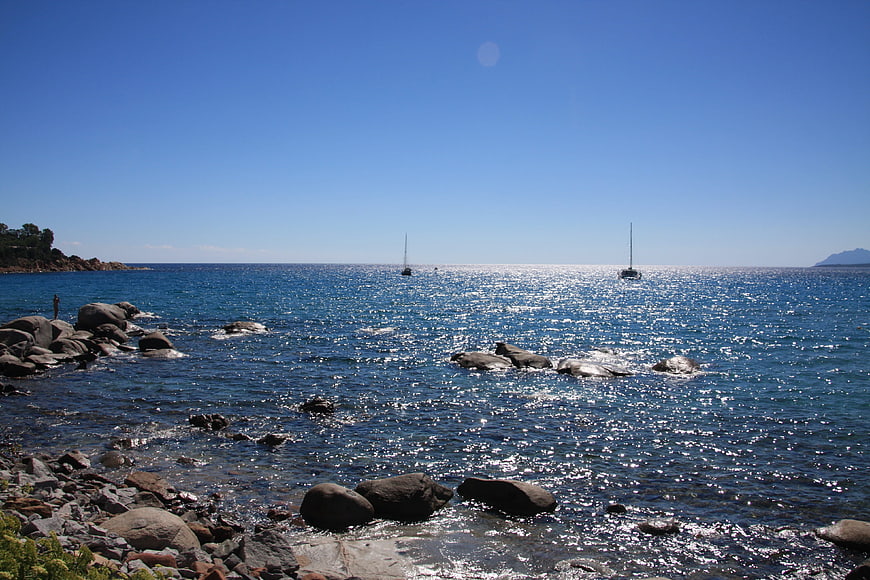 Sailboats on Sparkling Blue Sea with Rocky Shoreline