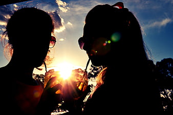 Silhouette of two women clinking cocktail glasses at sunset