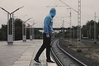 Man in blue hoodie walking on railway tracks