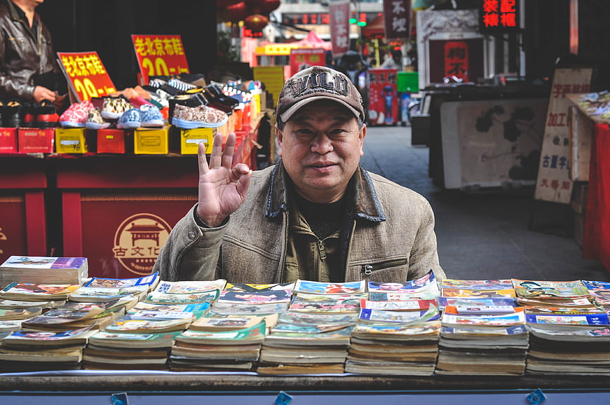 Friendly elderly Chinese man selling books at outdoor market
