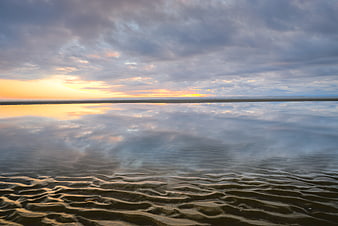 Serene sunset reflection on wet sandy beach with rippled texture