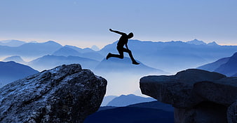 Silhouette of man jumping between rocks in mountain landscape