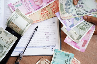 Indian Rupee Banknotes, Pen, and Ledger on Wooden Desk