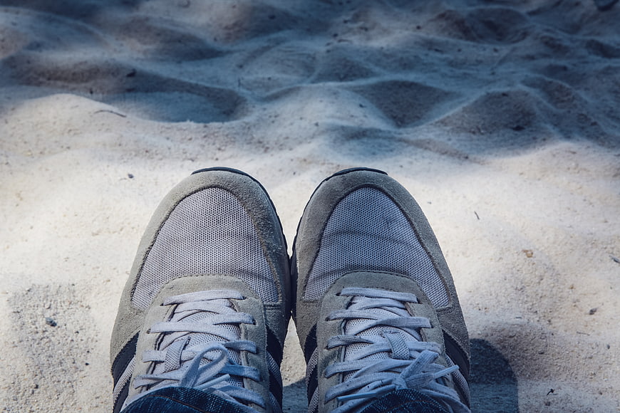 First-person view of grey sneakers on sandy beach