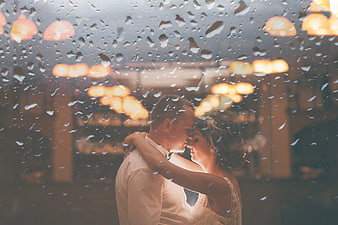 Romantic wedding couple dancing behind rain-streaked window