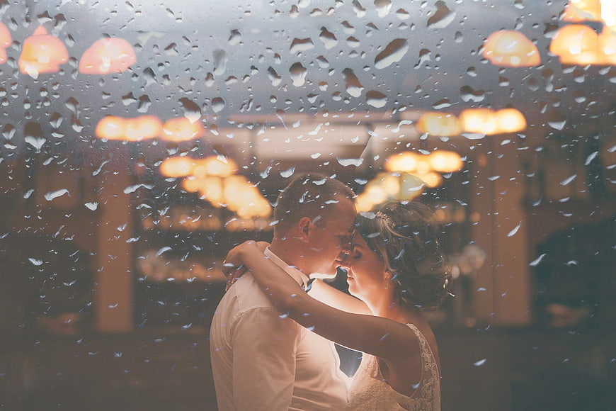 Romantic wedding couple dancing behind rain-streaked window