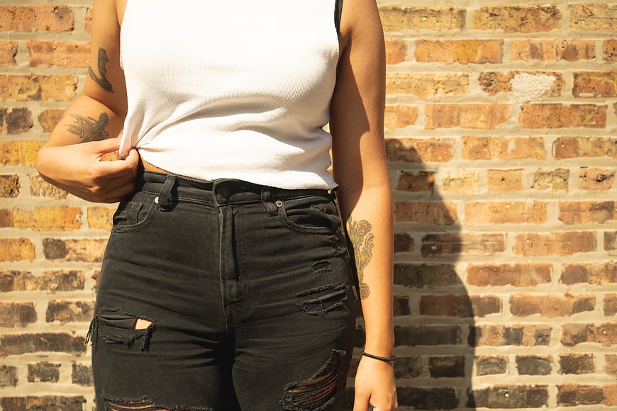 Woman in White Top and Ripped Jeans Against Brick Wall