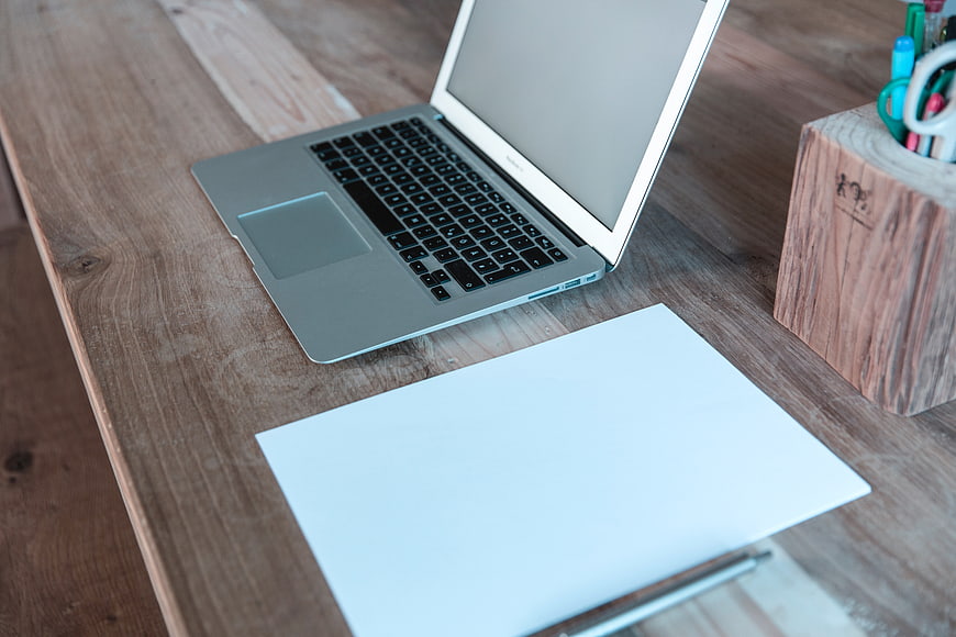 Laptop and blank paper on wooden desk workspace