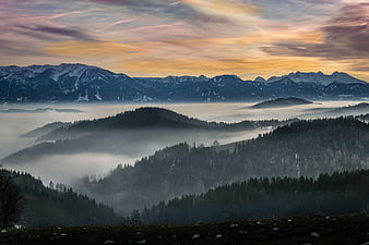 Misty mountain landscape with sunset clouds and forest
