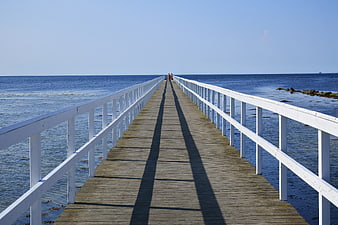 Long wooden pier extending into blue ocean with white railings