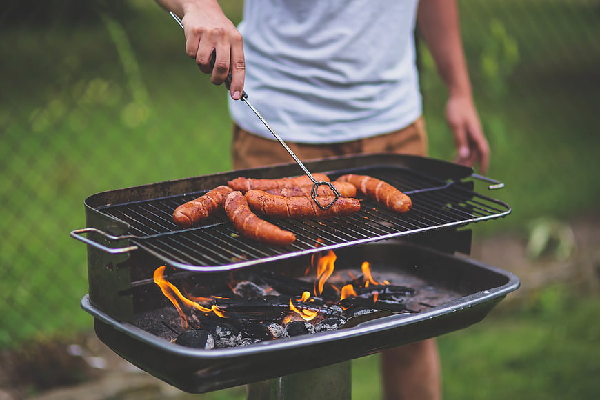 Man grilling sausages on charcoal barbecue outdoors