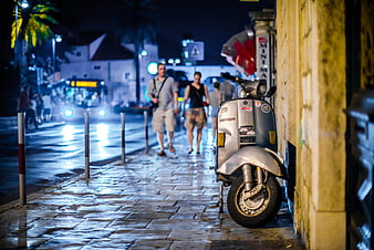 Silver Vespa Scooter Parked on Wet Cobblestone Street at Night