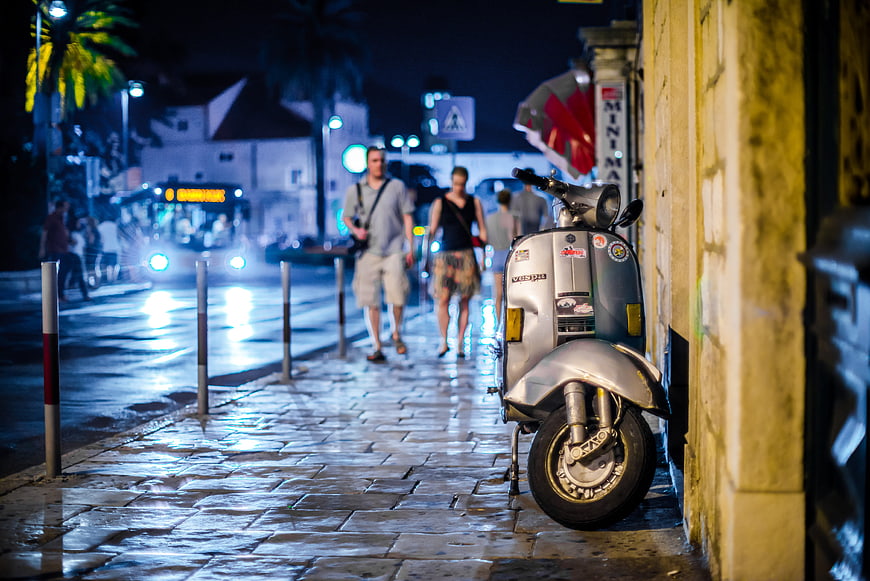 Silver Vespa Scooter Parked on Wet Cobblestone Street at Night